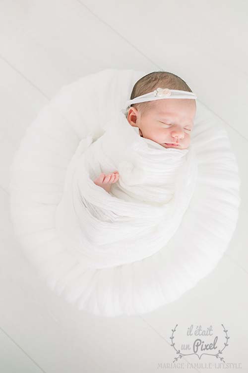 Newborn baby in a white wrap and in a white woolen nest during a studio photo session